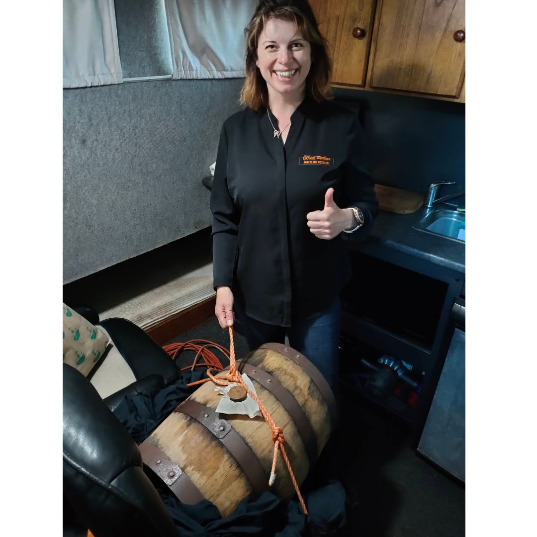Image description: Happy Heidi, the King Island Distiller and Deckhand, is standing in front of her barrel of King Island Gin being aged at sea on a Crayfish boat named Even Steven. She is posing with her thumb up.
